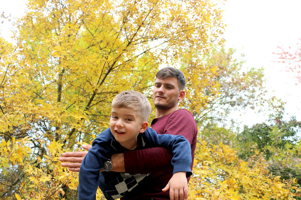 otec drží svého syna v jeho paže, otec a syn hrát spolu venku v lese - Fotografie, Obrázek
