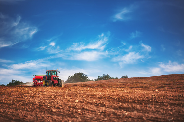 Farmer with tractor seeding crops at field - Foto, Bild