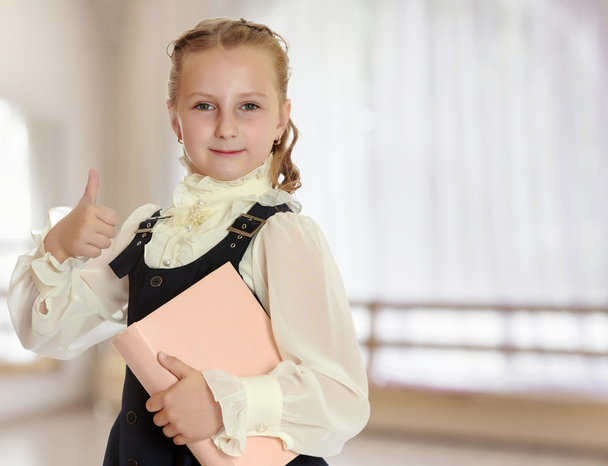 Girl schoolgirl with a book in hand shows thumb. - Φωτογραφία, εικόνα