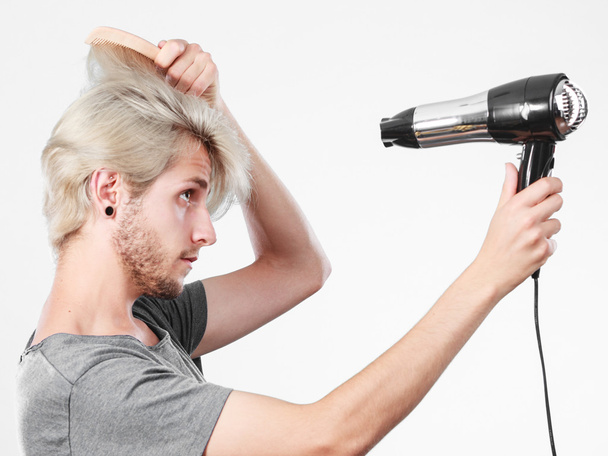 Young man drying hair with hairdryer - 写真・画像