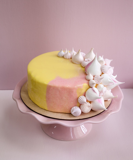 Rózsaszín mousse torta borított-val sárga és rózsaszín tükör csokoládé mázzal és habcsók csókok. A rózsaszín porcelán állást. Rózsaszín háttér. Természetes fény. - Fotó, kép