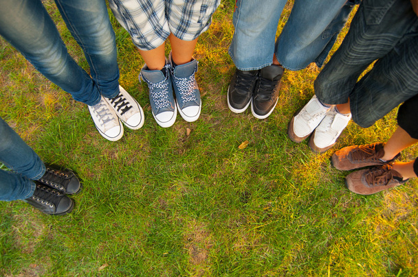 Pernas e tênis de meninos e meninas adolescentes em pé em meio círculo na grama
 - Foto, Imagem