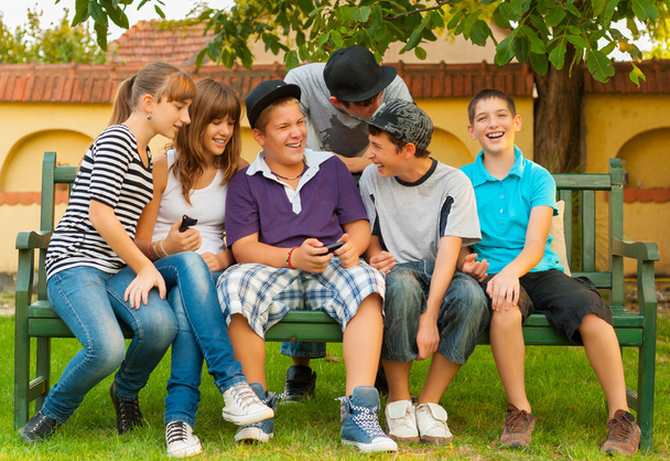 Teini-ikäiset pojat ja tytöt hauskaa puutarhassa istuessaan penkillä
 - Valokuva, kuva