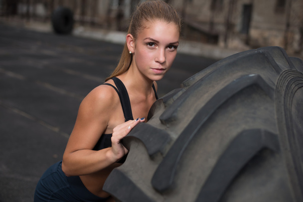 Jeune femme musculaire retournant pneu à la salle de gym. Fit athlète féminine effectuant un retournement de pneu à Crossfit gym
. - Photo, image