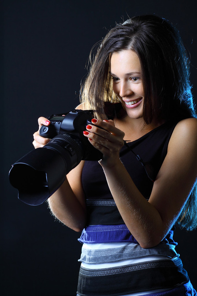 Woman with camera on a dark background looking at her great shot - Fotoğraf, Görsel