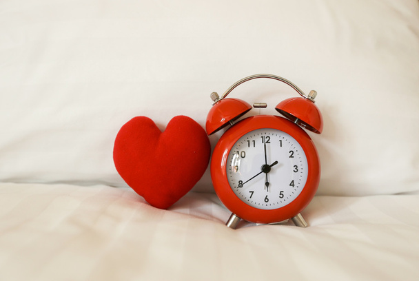 Red alarm Clock and heart shape on white bed sheet - Fotografie, Obrázek