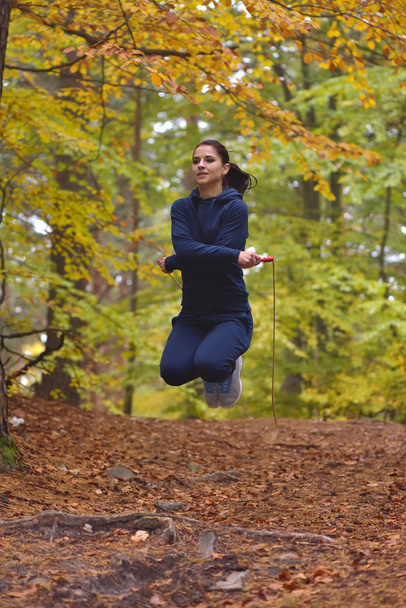 Young beautiful fitness woman skipping rope in forest, autumn colors - Photo, image