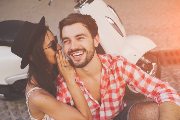 couple whipsering to ear a secret while sitting near scooter - Photo, Image