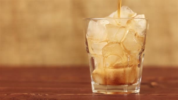 アイスとコーラ。木製のテーブルと茶色の背景にガラスの氷と泡とコーラを注ぐ - 映像、動画