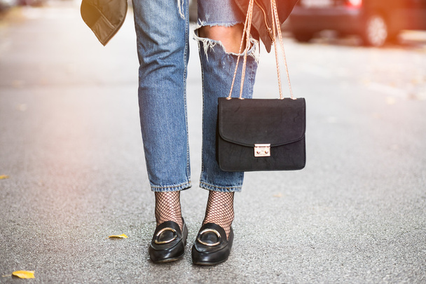 upadek strój moda szczegóły, młoda kobieta stylowe sobie zgrywanie dżinsy i czarne mokasyny. blogger moda gospodarstwa modne torebki czarne ze złotym łańcuchem. - Zdjęcie, obraz