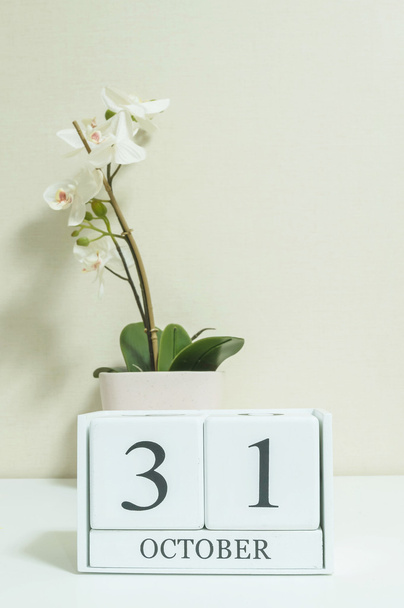 Closeup white wooden calendar with black 31 october word with white orchid flower on white wood desk and cream color wallpaper in room textured background , selective focus at the calendar - Φωτογραφία, εικόνα