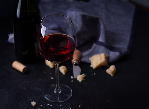 Glass of red wine, cheeses and cheese knife on black background - Foto, Bild