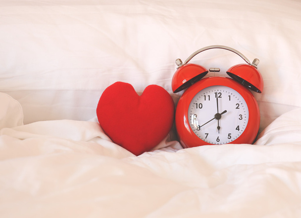 Red alarm Clock and heart shape on white bed sheet - Photo, Image