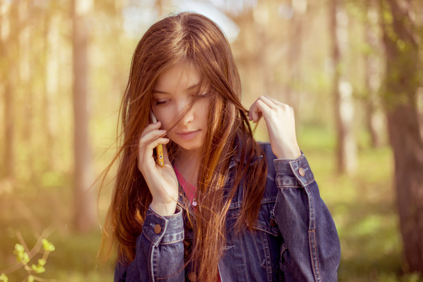 La chica con el pelo largo y liso castaño en una chaqueta de mezclilla habla o
 - Foto, imagen