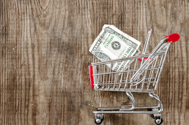 Cart from the grocery store and money on wooden background. Retail trade and advertising. Purchase in the store. - Φωτογραφία, εικόνα
