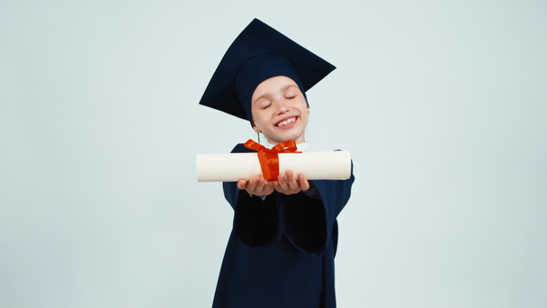 Portre mutlu öğrenci kız manto holding 7-8 yılda mezun ve onun diploması sevinir. Çocuk dişleri beyaz arka plan üzerinde gülümseyen - Video, Çekim