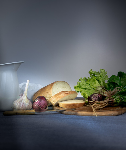 still life. jug, bread, onion, garlic, spinach on a blue tablecloth. space for text - 写真・画像