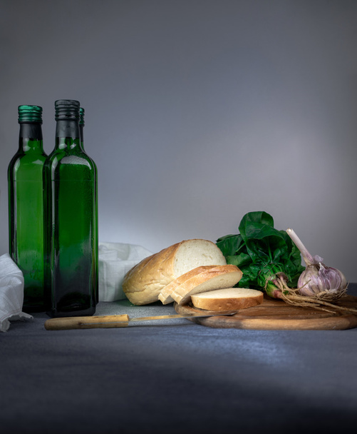 still life. bottle, bread, garlic, spinach on a blue tablecloth. space for text - Фото, зображення