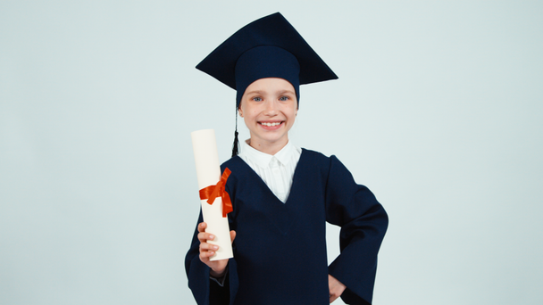 Portrait happy student graduate girl 7-8 years in mantle rejoices and indulges with her diploma and smiling with teeth on white background - Imágenes, Vídeo