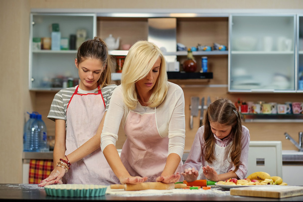 Mère enseignant à ses filles comment préparer la pâte
 - Photo, image