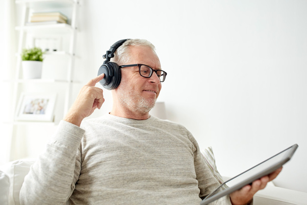 Starszy człowiek z komputera typu tablet i słuchawki w domu - Zdjęcie, obraz