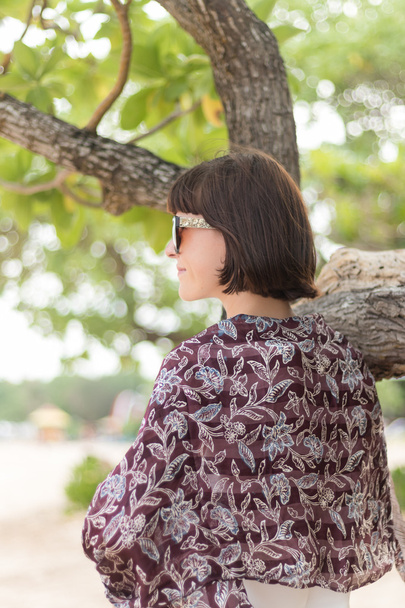Ritratto di bellezza di donna bruna sexy in abito bianco sulla spiaggia con foulard di seta colorata e occhiali da sole. Crociera moda estate. Bali, Indonesia
. - Foto, immagini