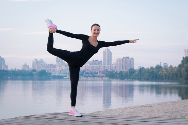 Young woman exercises on pier during morning training workout - Φωτογραφία, εικόνα