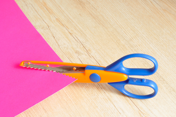 Ένα πολύχρωμο ψαλίδι Κόψτε μια τεθλασμένη μοτίβο με ένα ροζ χαρτί  - Φωτογραφία, εικόνα
