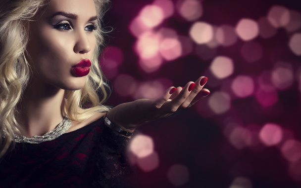 Beautiful blond woman blowing on his hand on background of festive lights. - Photo, Image
