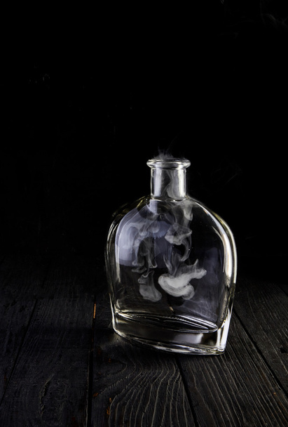 Empty decanter with smoke on black background - Φωτογραφία, εικόνα