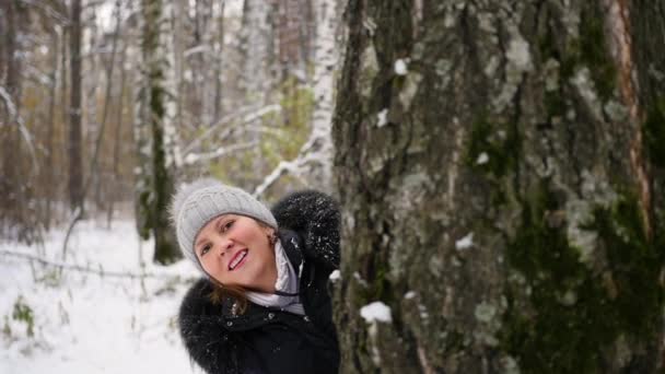 dziewczyna gra przez rzucanie śnieżkami zza drzewa w parku zimowym - Materiał filmowy, wideo