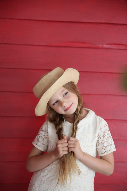red-haired girl wearing white dress with a hat on the background of red wooden wall - Foto, imagen