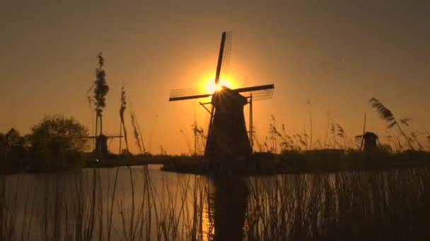 tradycyjnych wiatraków na brzegu rzeki o zachodzie słońca - Materiał filmowy, wideo