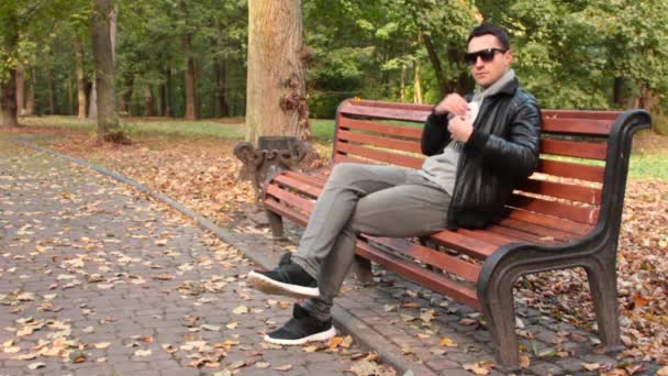 Mężczyzna, rozmawiając i śmiejąc się na telefon komórkowy siedząc na ławce w parku. - Materiał filmowy, wideo