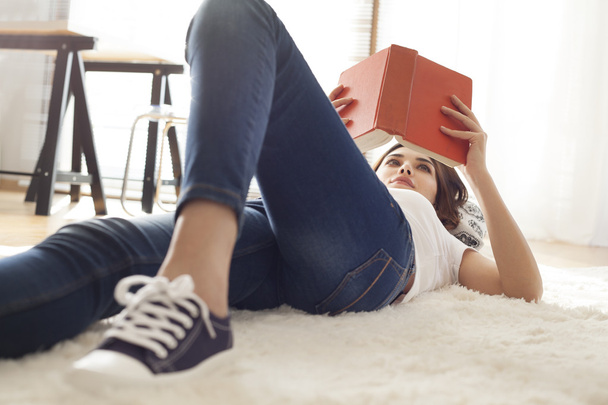 Young woman reading book on carpet - Zdjęcie, obraz