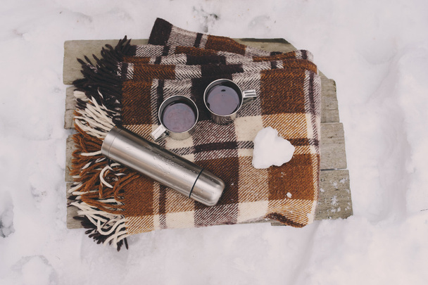冬雪の上でピクニック。居心地のよい暖かい毛布に熱いお茶、ポットと雪だるま心。季節のアウトドア. - 写真・画像