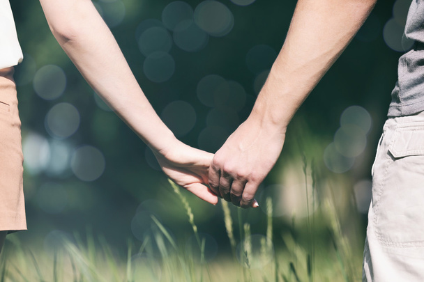 Young couple holding hands together on blurred nature background - Foto, Imagem