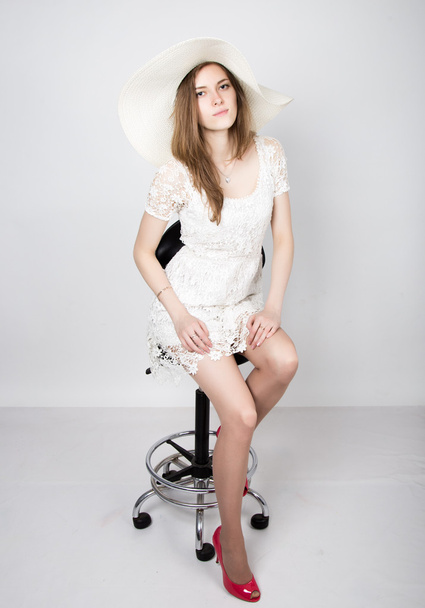 Beautiful young woman wearing a white dress and high heels, sitting on a chair. - Foto, Bild