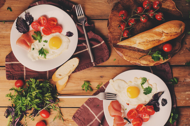top view of fried eggs with tomato, basil and prosciutto, table set for two, cozy breakfast at home - Foto, immagini