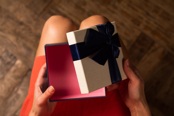  Frau öffnet einen Geschenkkarton mit blauem Band - Foto, Bild