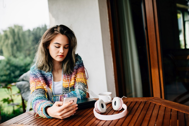 Woman in woolen sweater uses a smartphone on terrace. - Foto, afbeelding