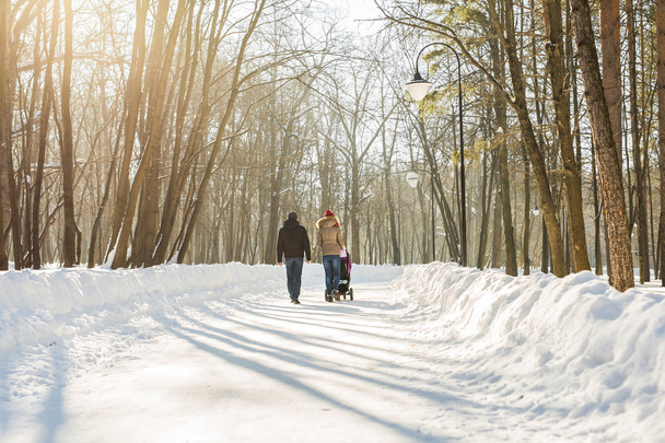 Szczęśliwe rodziny młodych spaceru w parku w zimie. Rodzice nosić dziecko w wózek przez śnieg. - Zdjęcie, obraz