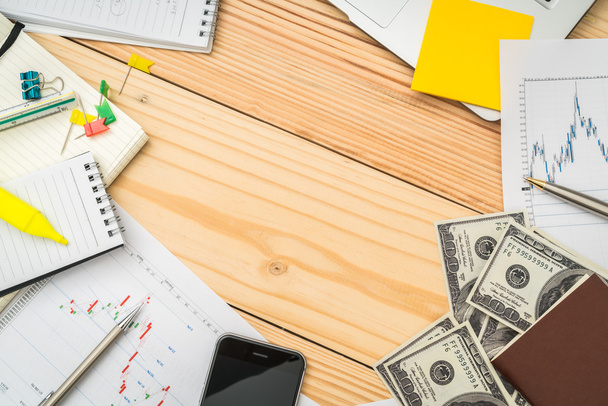 Фінансові графіки на столі з ноутбуком, телефоном, доларовим банком
 - Фото, зображення
