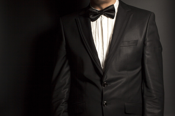 man wearing a black suit and bow tie on black background - 写真・画像