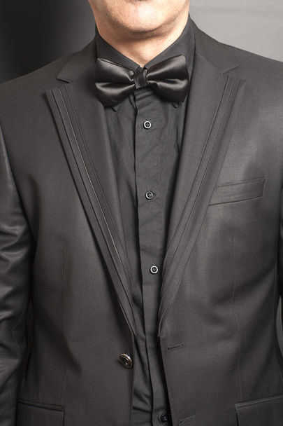 Mann trägt schwarzen Anzug und Fliege auf grauem Hintergrund - Foto, Bild