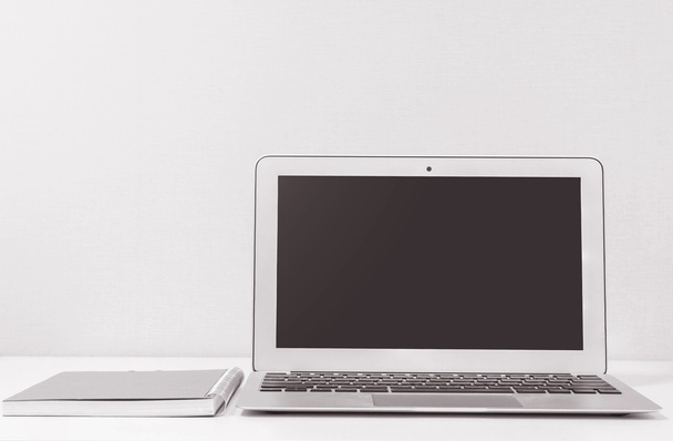Vértes számítógép notebook homályos fehér fa íróasztal és krém színű tapéta fal a szoba textúra háttér, gyönyörű munkahelyi belső house koncepció, fekete-fehér hang - Fotó, kép