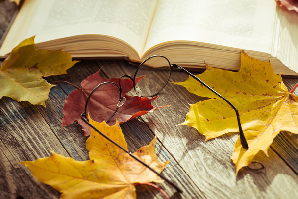 Eye glasses with book and autumn leaves on table - Foto, afbeelding