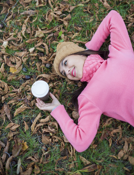 Girl lying on autumn leaves with coffee looking away - Fotografie, Obrázek