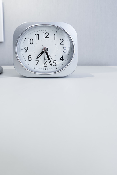 white square clock on white bed stand with white wallpaper background, morning time in minimal style decoration. - Φωτογραφία, εικόνα