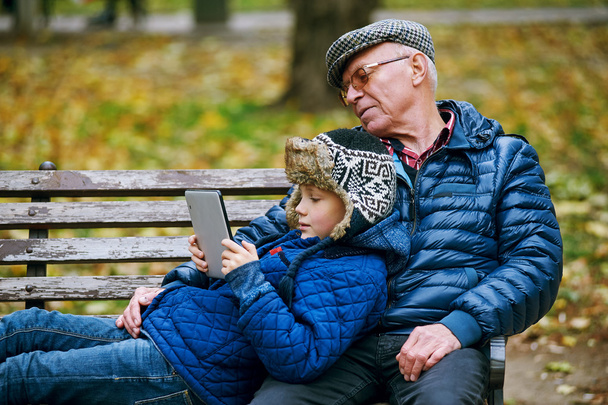 Grandson with grandfather in the autumn Park and read using a tablet - Fotoğraf, Görsel